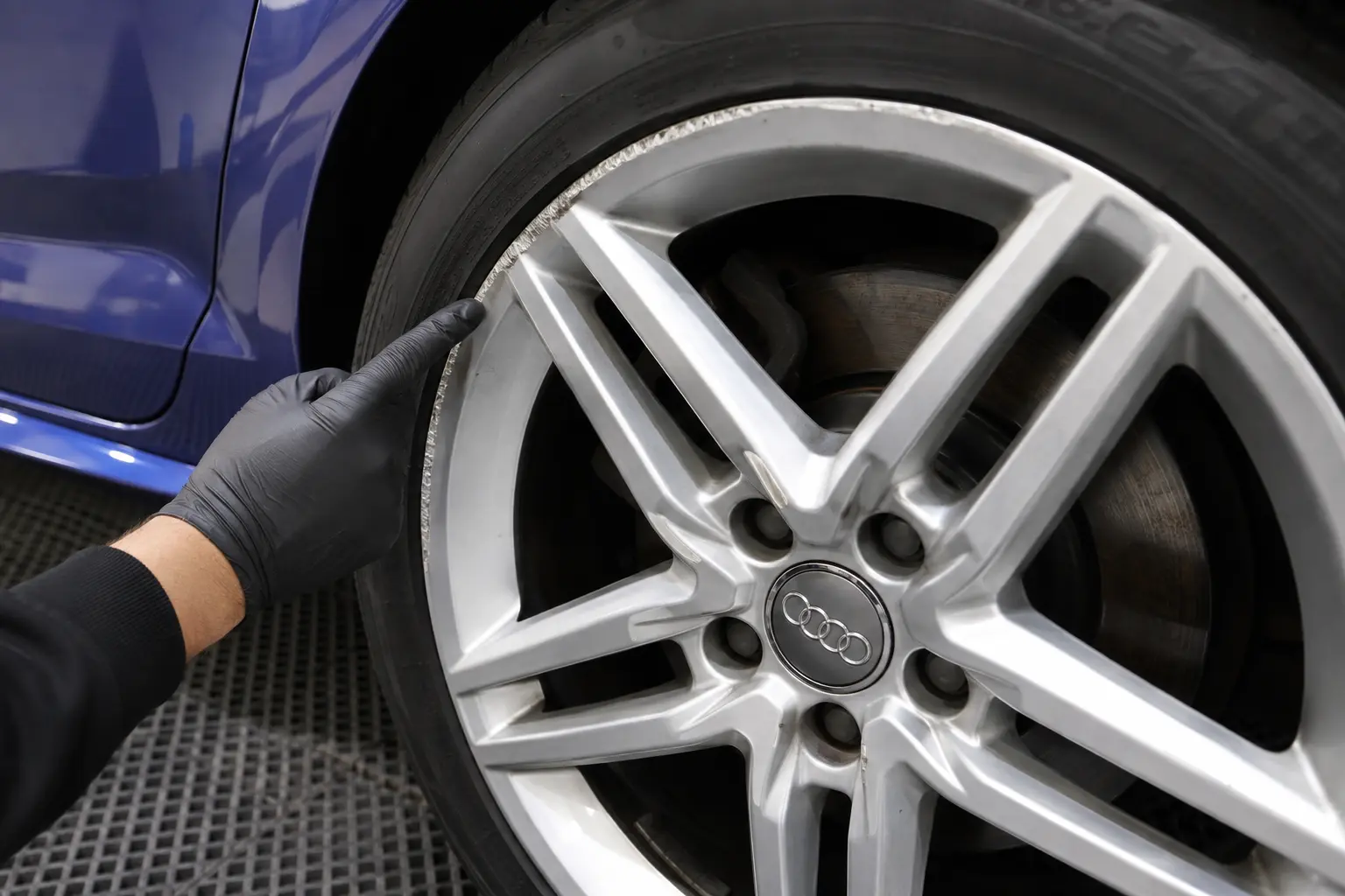 Technician inspecting kerb rash on a silver Audi alloy wheel