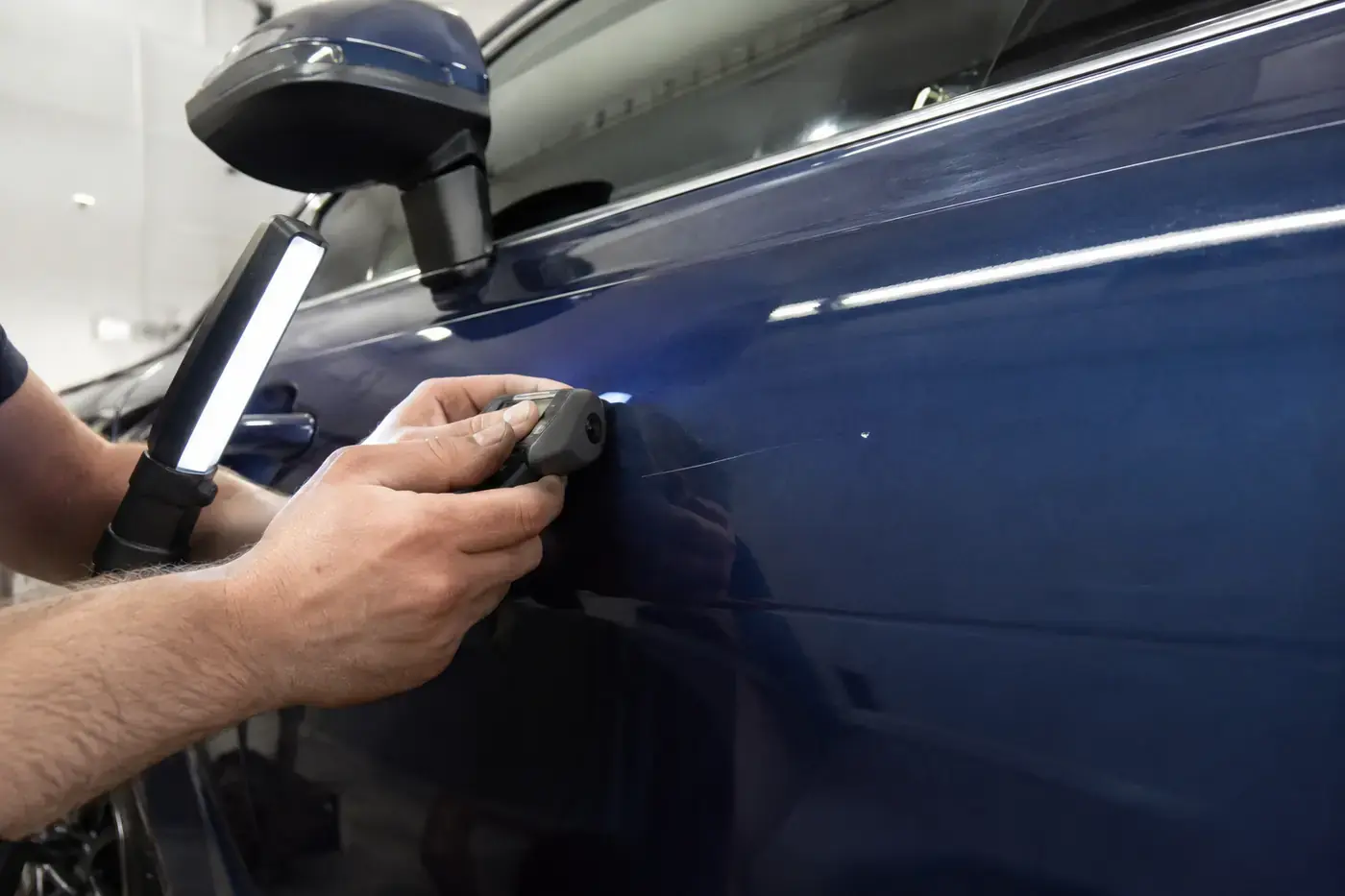 Technician checking scratch depth and coating thickness on a blue Audi door