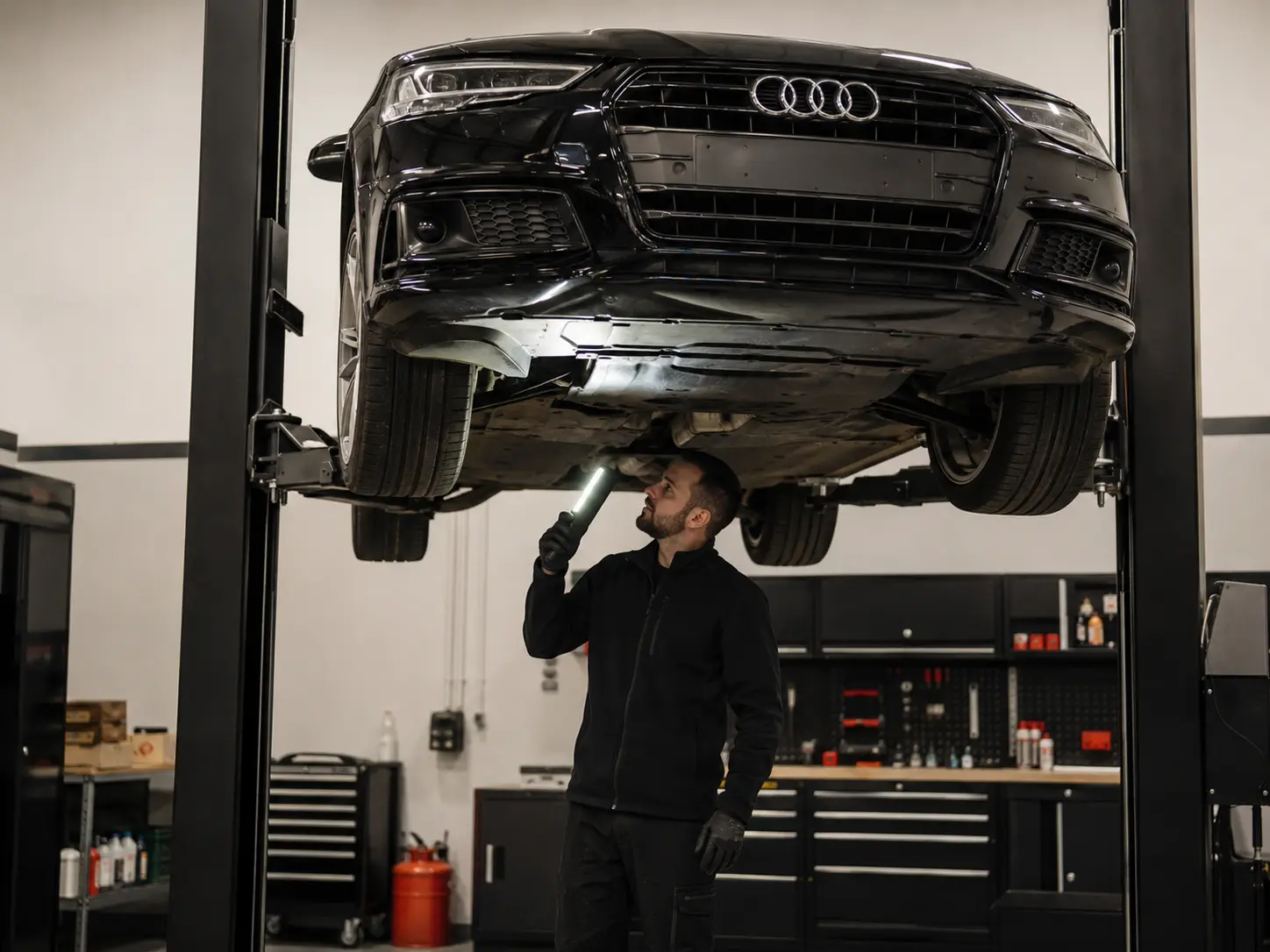 Technician inspecting the underside of a raised Audi with a lamp