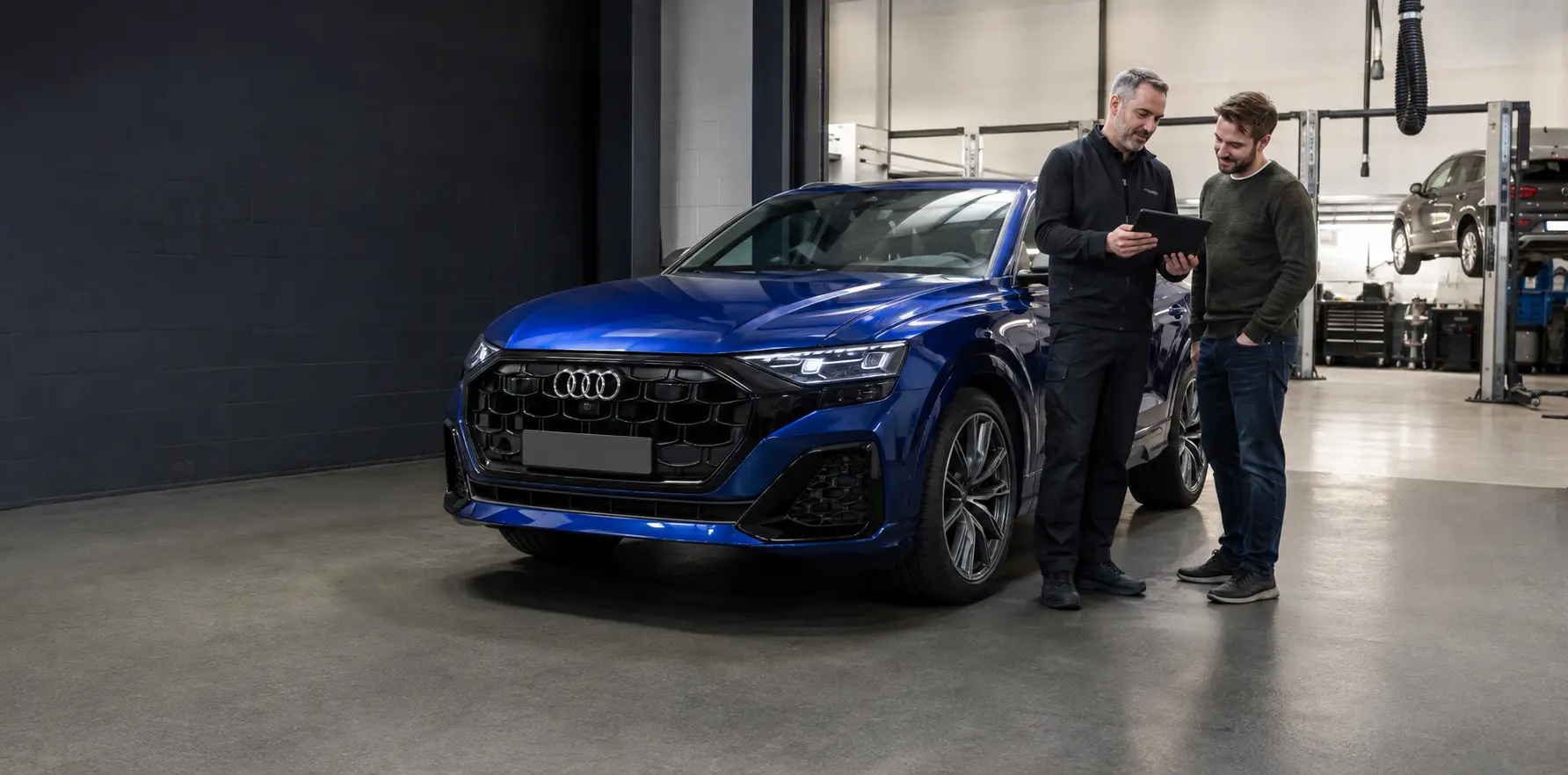 Ultra Blue Audi Q8 with an owner and workshop adviser reviewing inspection details