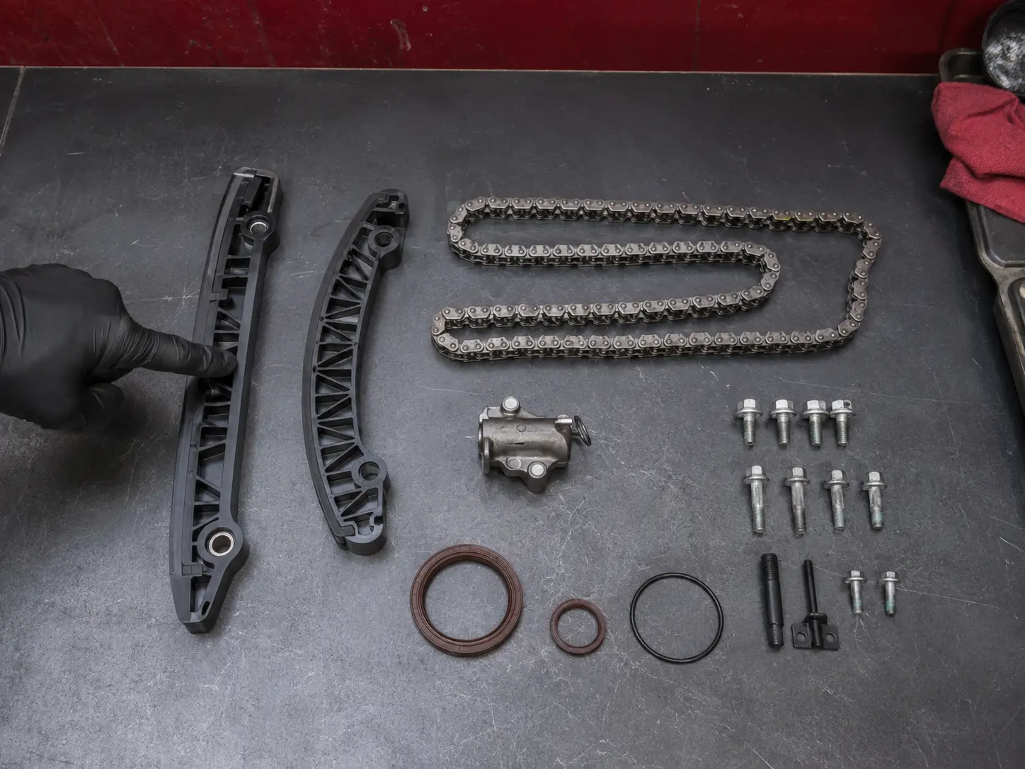 Timing chain, guides, tensioner, seals and fasteners arranged on a workshop bench